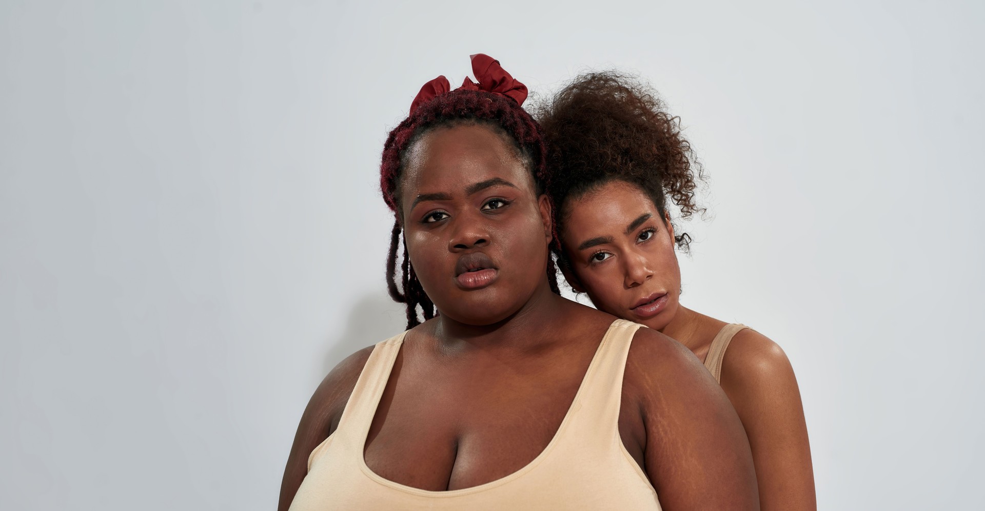 Portrait of two friends african american women with different body size looking at camera, posing together isolated over gray background